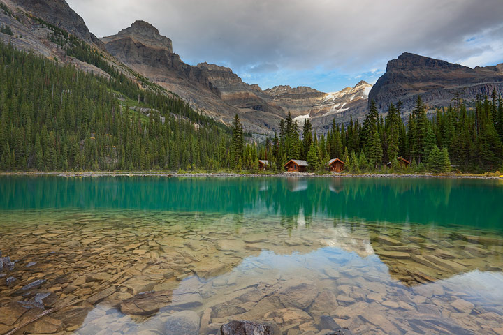 Mount Lefroy and Glacier peaks tower over the deluxe cabins reflecting in the turquoise waters of Lake O'Hara.<br />