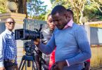 Man in blue sweater holding black dslr camera