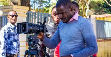 Man in blue sweater holding black dslr camera